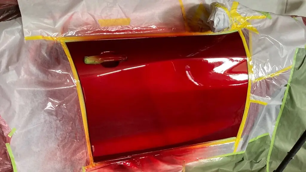 Door panel masked off with fresh red basecoat in the paint booth