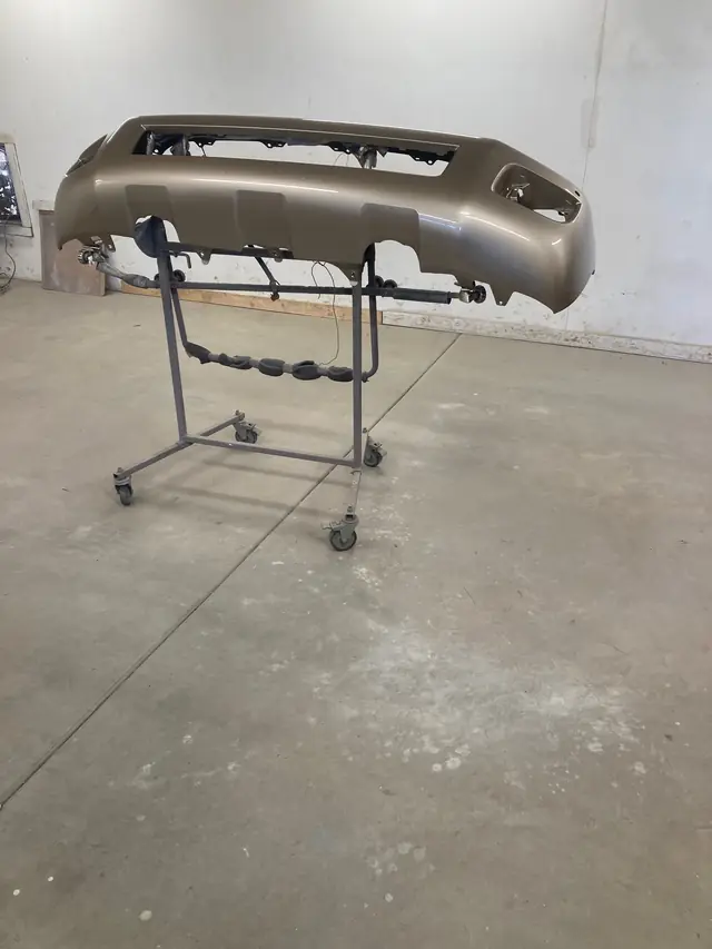 Tan bumper cover on a paint stand in an empty bay