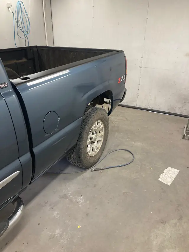 Blue-grey Chevy truck bed side in the repair bay