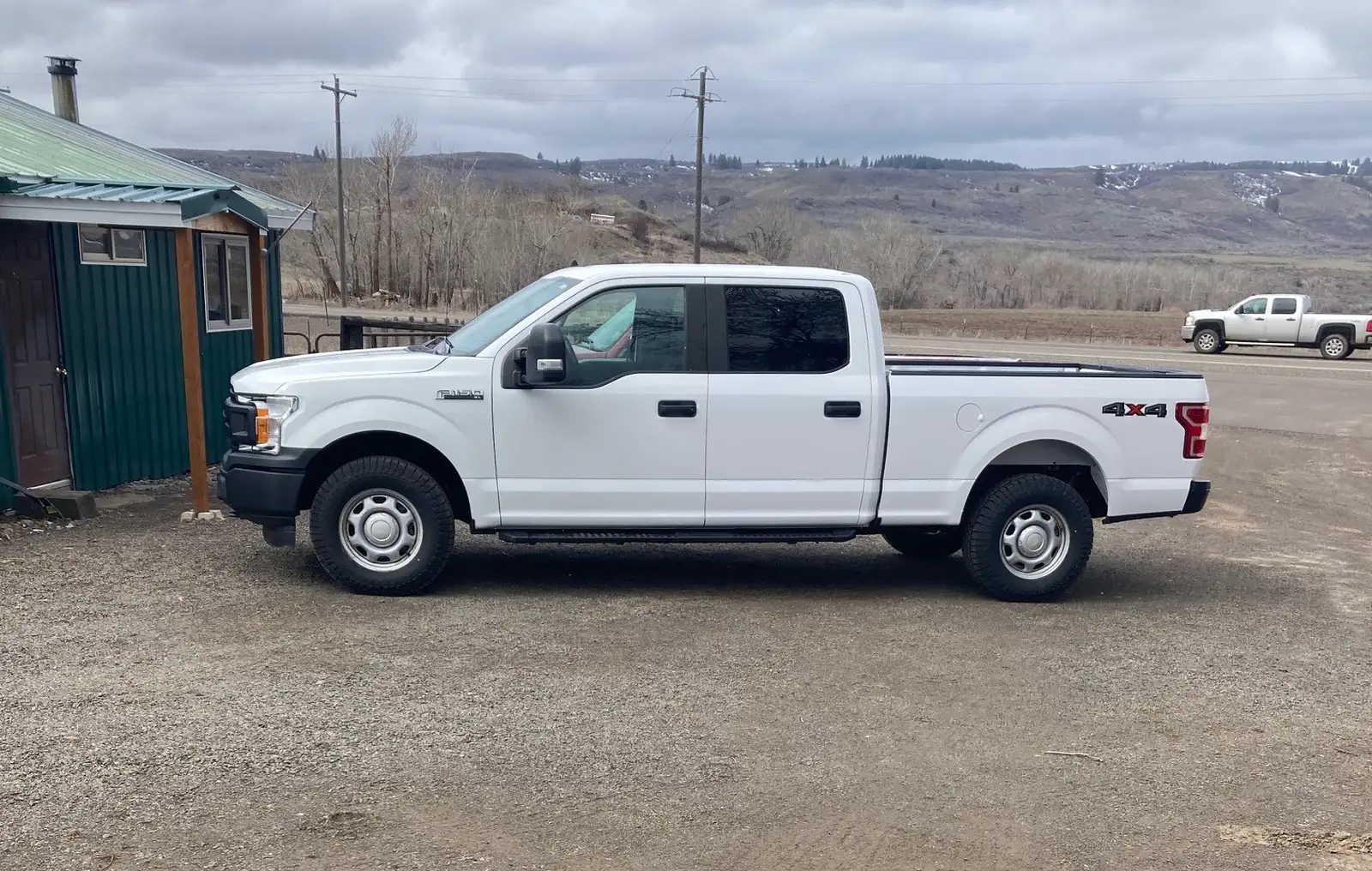 White pickup in the shop's gravel yard beside the green-roofed building, hills behind