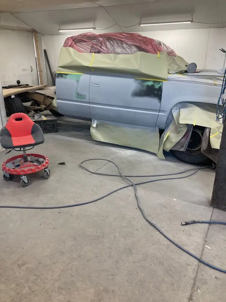 Pickup half-primed under masking paper in the paint booth, a creeper on the floor